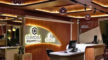 Uma área de recepção com design moderno, com um balcão de madeira, um display digital e uma placa com a inscrição 'DIMORA HOTELS & RESORTS aura 42'.