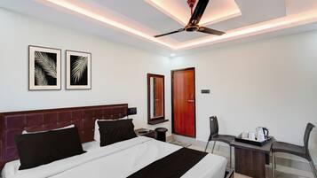 A hotel room with a bed, a desk with a chair, a ceiling fan, and two framed wall art pieces.