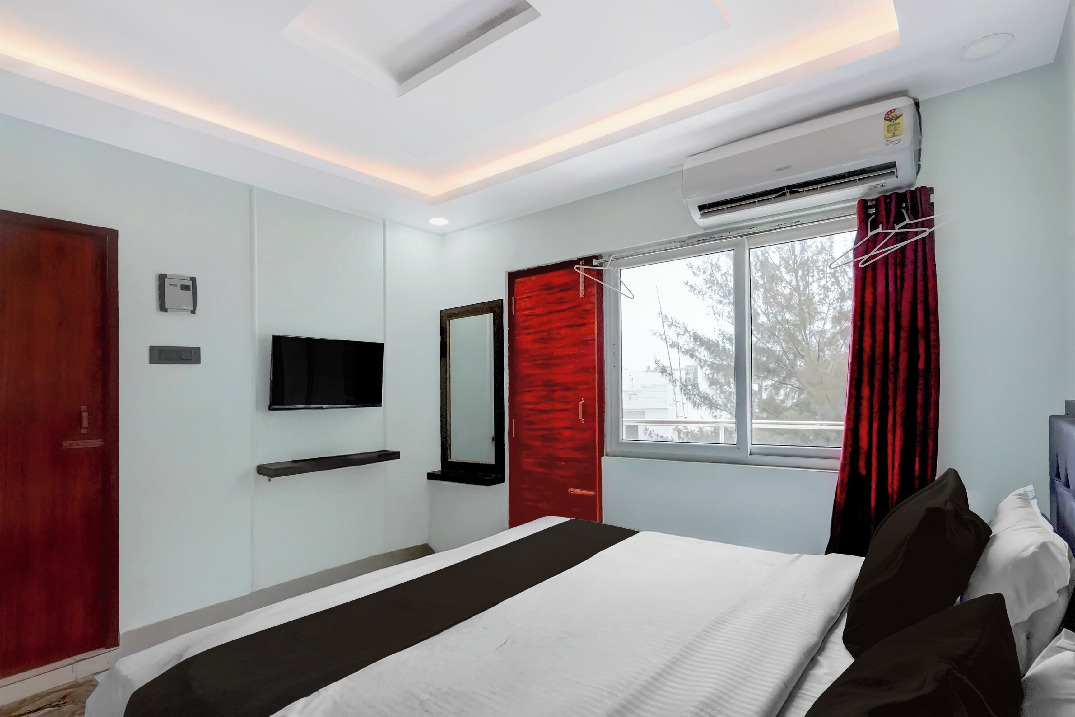 Ein Hotelzimmer mit einem Bett, einem Fernseher, einem Fenster mit Vorhängen und einer Klimaanlage.