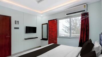 Ein Hotelzimmer mit einem Bett, einem Fernseher, einem Fenster mit Vorhängen und einer Klimaanlage.