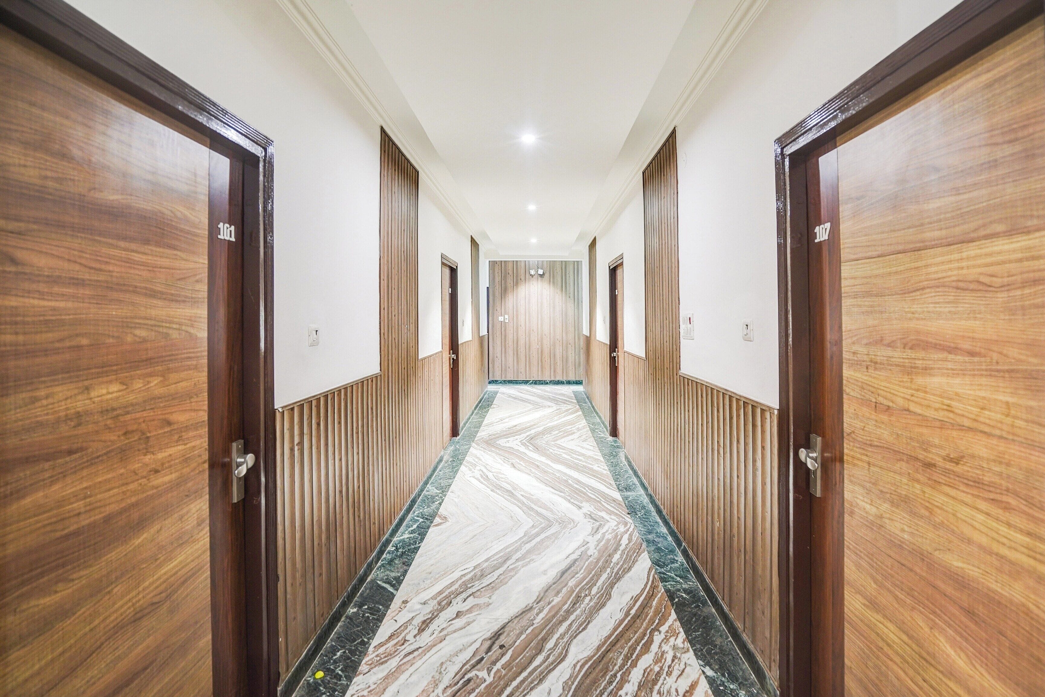 A hotel corridor with wooden doors, a marble floor, and a ceiling with recessed lighting.