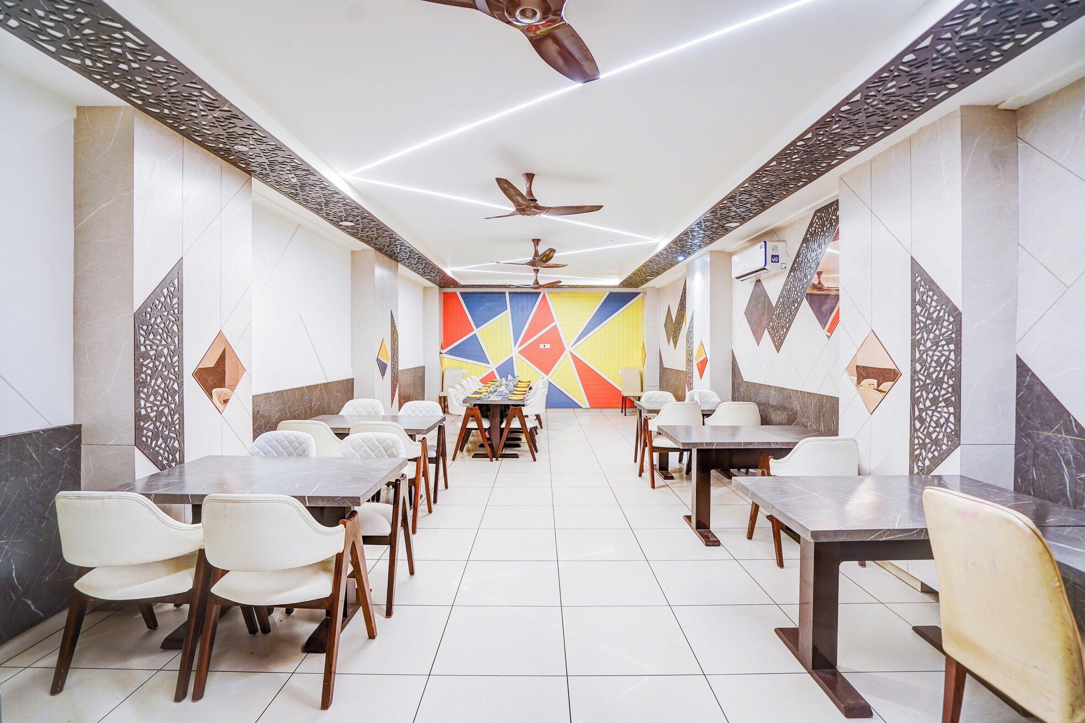 A modern dining area with multiple tables and chairs, ceiling fans, and decorative wall panels.