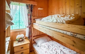 A bunk bed room with a wooden headboard, a bedside table with a clock, and a window with patterned curtains.