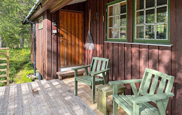 A wooden cabin with a porch, two green chairs, and a bench.