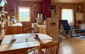 Ein Holzblockhaus-Interieur mit Esstisch, Stühlen, einer Küchenzeile und einem Schaukelstuhl.