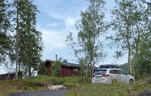 A cabin with a red exterior, surrounded by trees and a parked car.