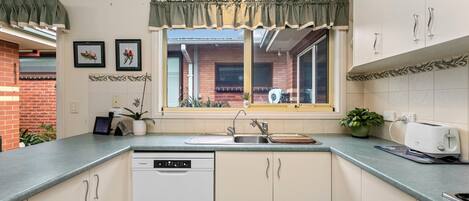 A kitchen with a dishwasher, a sink, and a window with a view of a brick building.