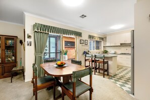 A dining area with a wooden table and chairs, a bowl of fruit, and a view of the kitchen. - Beach retreat.
Cosy two bedroom villa, with every box ticked opposite the beach. (Seaholme)