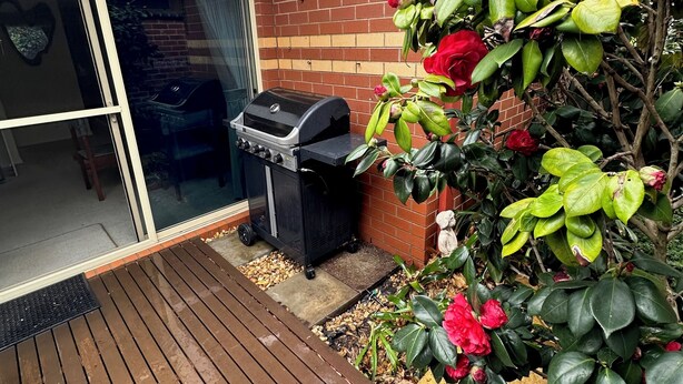 Eine Terrasse mit Grill, einer Glasschiebetür und einer Backsteinmauer.