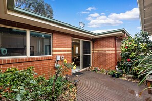A residential property with a brick facade, a sliding glass door entrance, a wooden deck, and a variety of plants and shrubs. - Beach retreat.
Cosy two bedroom villa, with every box ticked opposite the beach. (Seaholme)