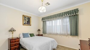 Ein Schlafzimmer mit einem Bett, zwei Nachttischen, einer Lampe, einem Gemälde und einem Fenster mit Vorhängen.