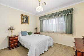 A bedroom with a bed, two nightstands, a lamp, a painting, and a window with curtains. - Beach retreat.
Cosy two bedroom villa, with every box ticked opposite the beach. (Seaholme)