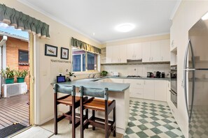A kitchen with a central island, white cabinets, a stainless steel refrigerator, and a checkered floor pattern. - Beach retreat.
Cosy two bedroom villa, with every box ticked opposite the beach. (Seaholme)