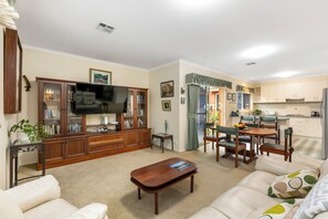 A living room with a television, a dining area with a table and chairs, and a kitchen with cabinets and appliances. - Beach retreat.
Cosy two bedroom villa, with every box ticked opposite the beach. (Seaholme)