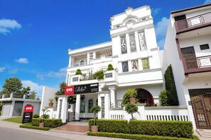 A white building with a classical architectural style, featuring a central entrance with columns, a balcony, and a sign for the OYO Collection. - Collection O Rudrapur Bus Stand Formerly (Rudrapur)