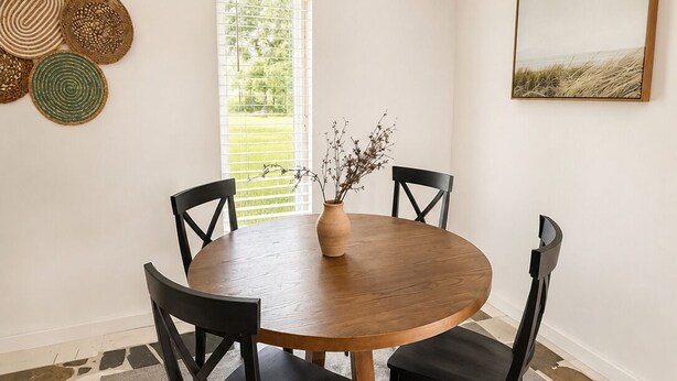 A dining area with a round wooden table, four black chairs, a vase with dried plants, and a painting on the wall. - Lakefront Studio Near Universal & Sea world (Orlando)