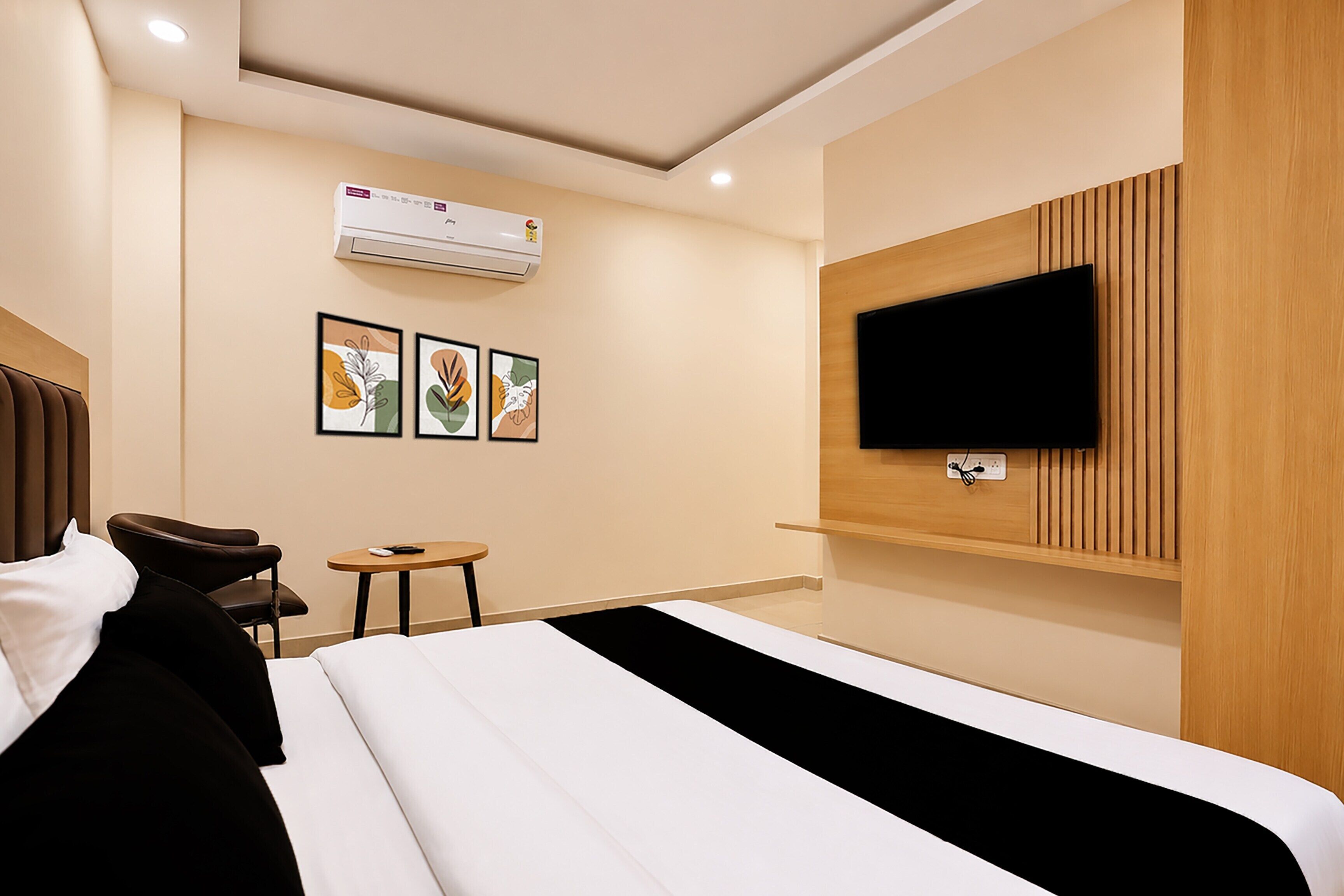 A hotel room with a bed, a TV mounted on the wall, a small table, and two framed artworks.