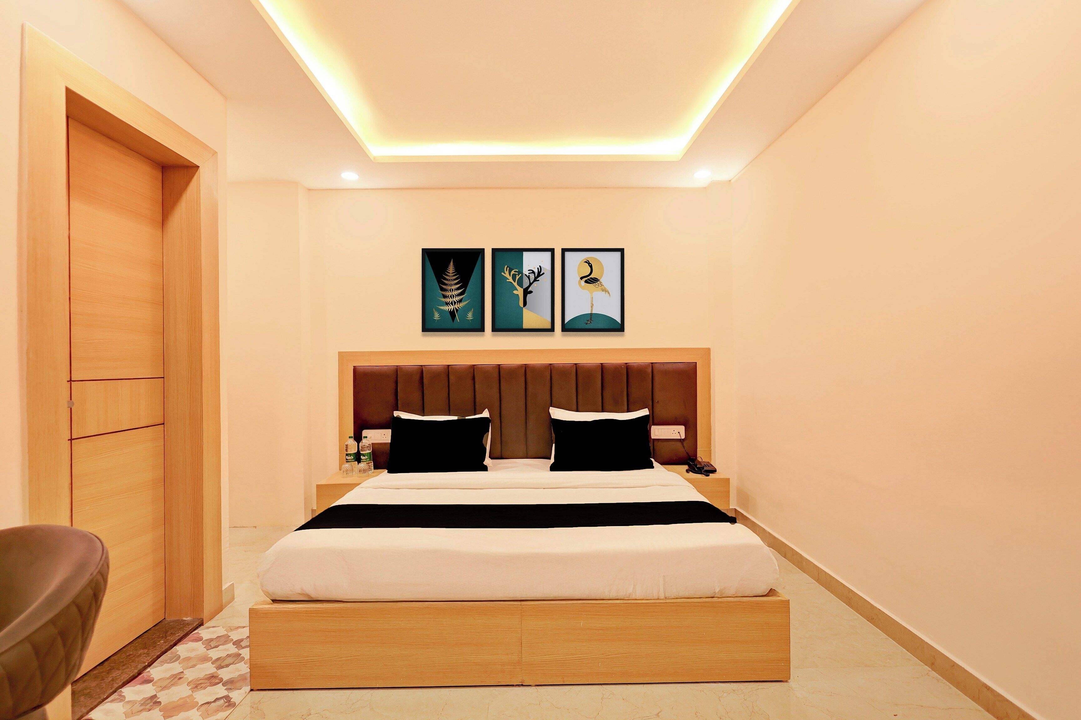 Habitación de hotel con cama, cabecera, mesita de noche, una silla y cuadros en la pared.