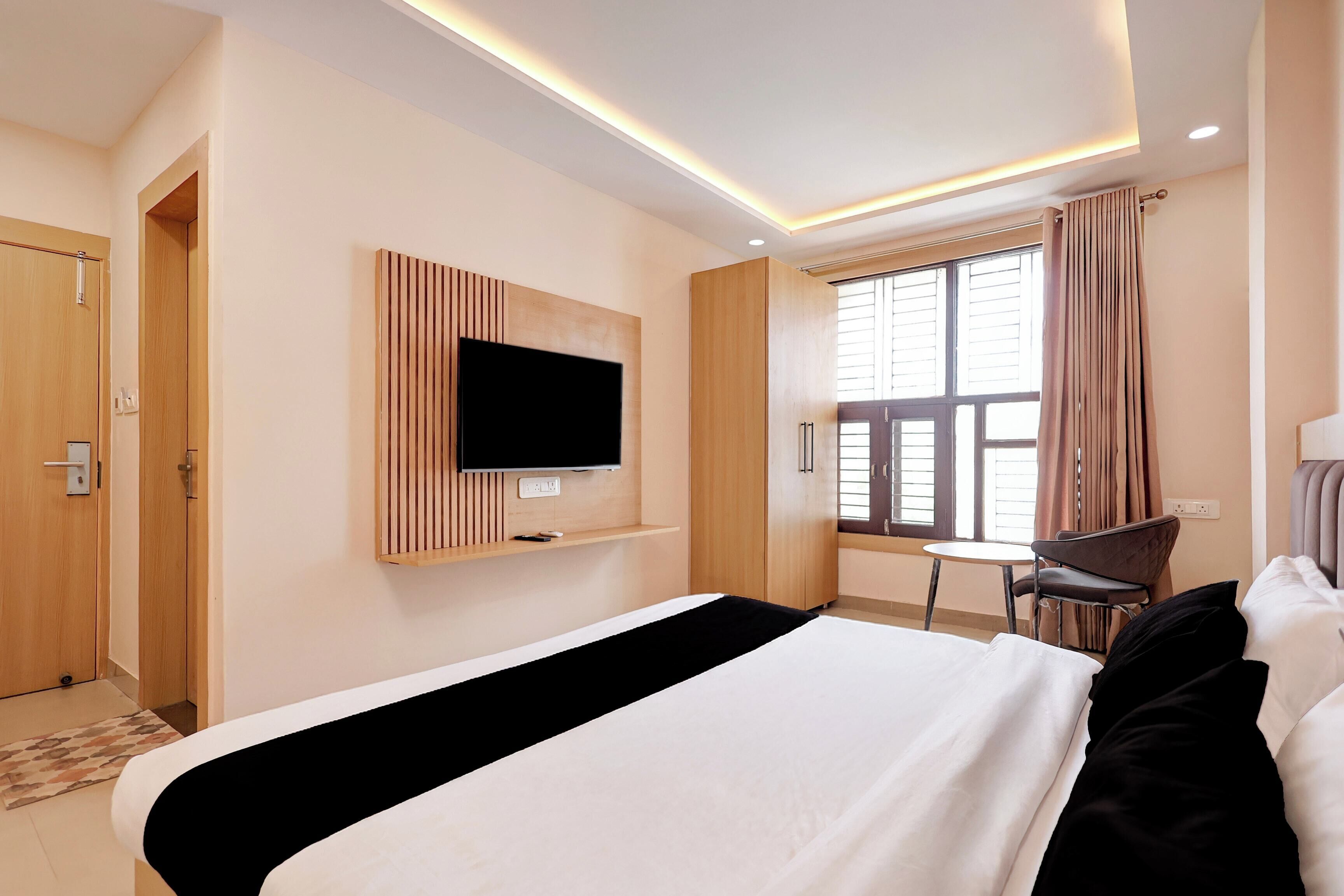 A hotel room with a bed, a TV mounted on the wall, a window with curtains, and a chair.
