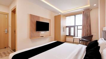 A hotel room with a bed, a TV mounted on the wall, a window with curtains, and a chair.
