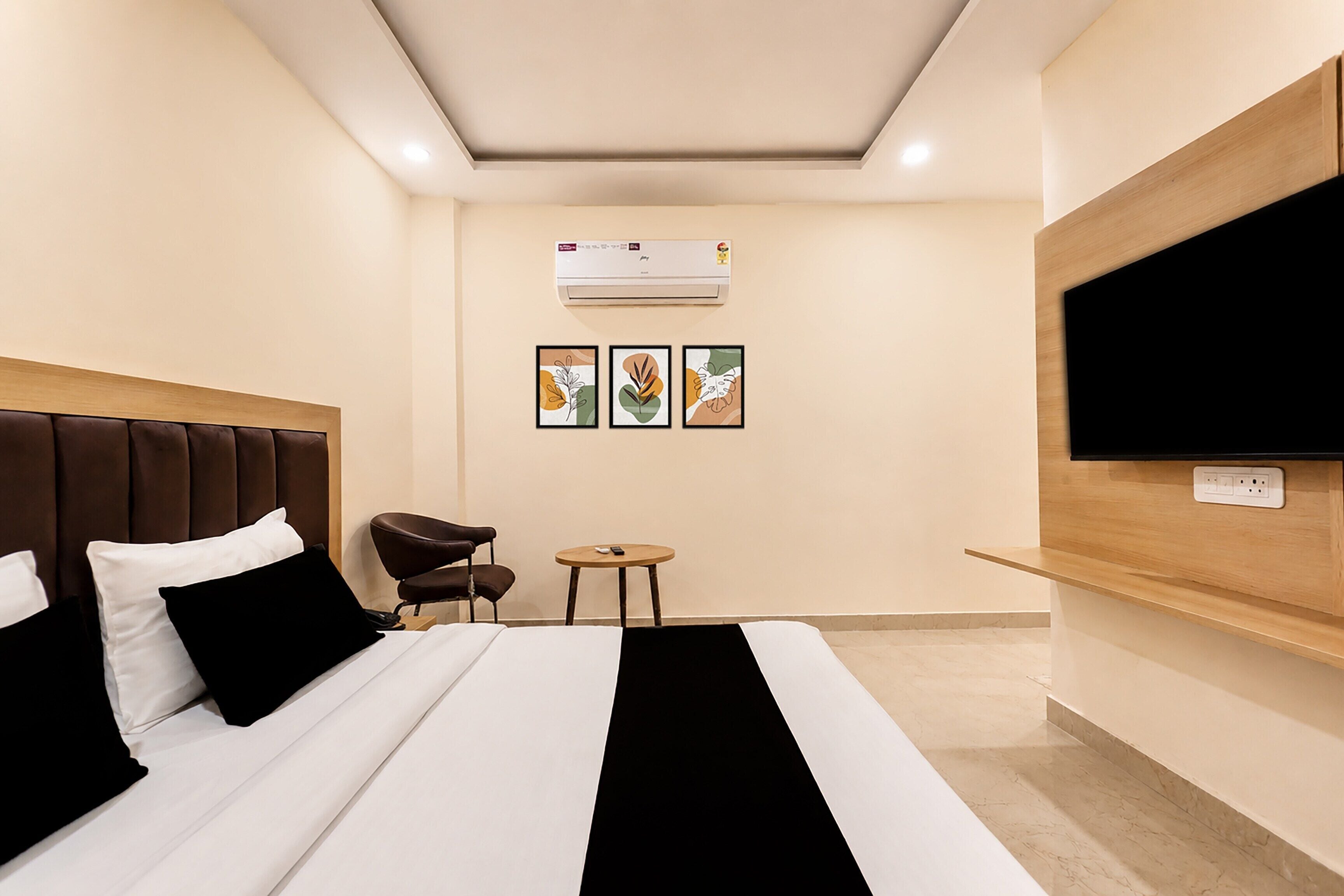 Una habitación de hotel con una cama, una silla, una mesita pequeña, un equipo de aire acondicionado y un televisor montado en la pared.