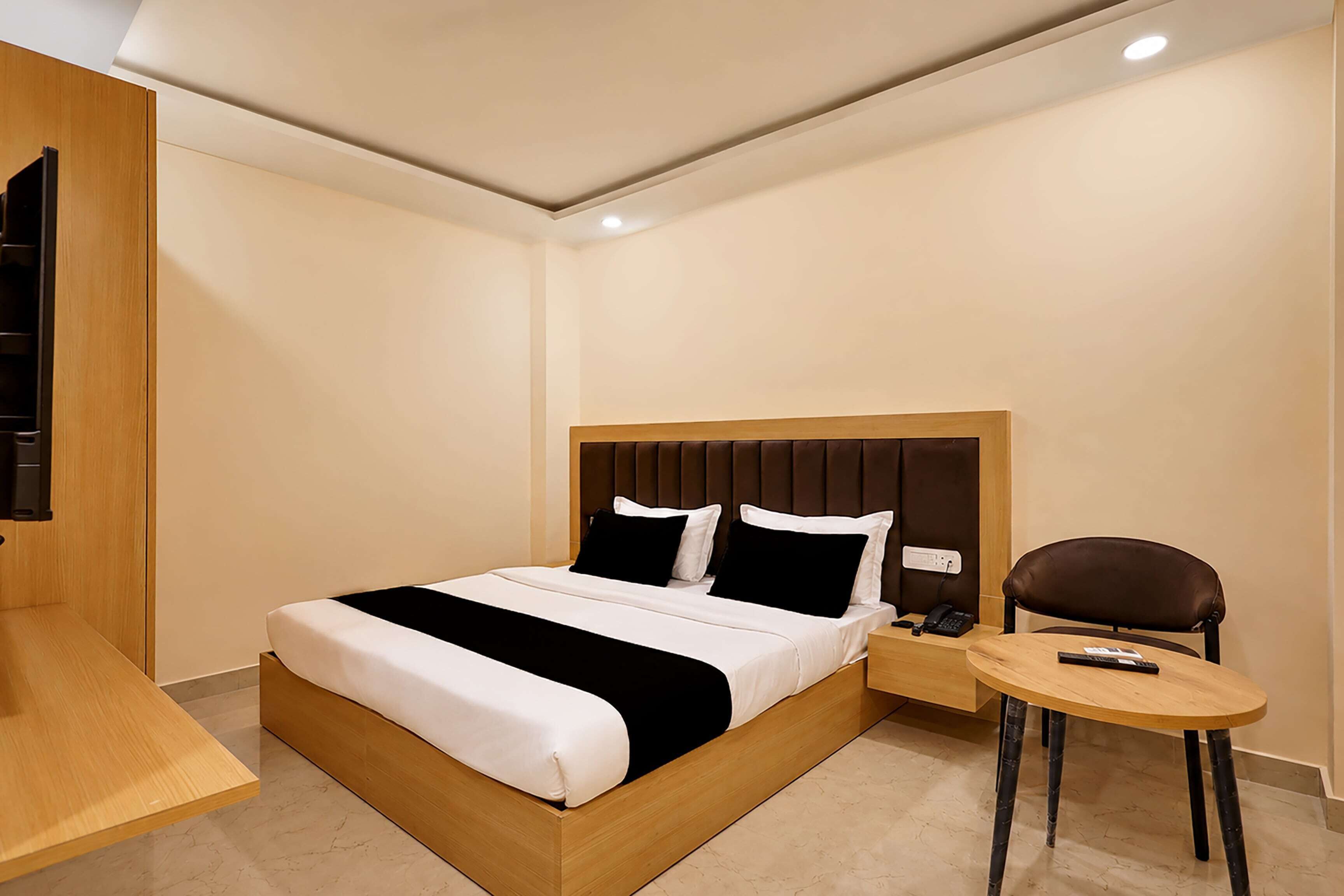 Habitación de hotel moderna con una cama de madera, una mesita de noche, una silla y un escritorio pequeño.