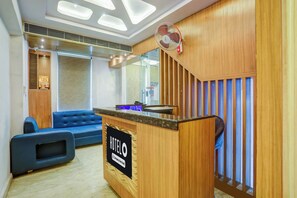 Zona de recepción de un hotel con un sofá azul, un mostrador de recepción y una pared de madera con listones verticales.