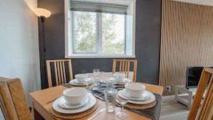 A dining table set with plates, bowls, glasses, and cutlery, with a window and blinds in the background. - Free Parking 2BR Sleeps 5 Close to JR Hospital (Oxford)