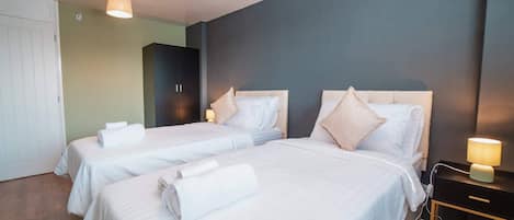 A hotel room with two beds, a wardrobe, a desk with a lamp, and a wall clock.