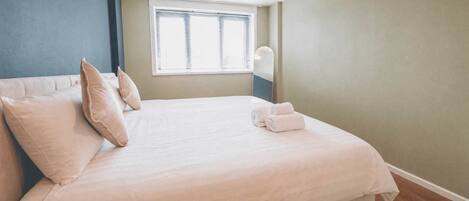 A neatly made bed with pillows and towels, a window with blinds, and a pendant light.