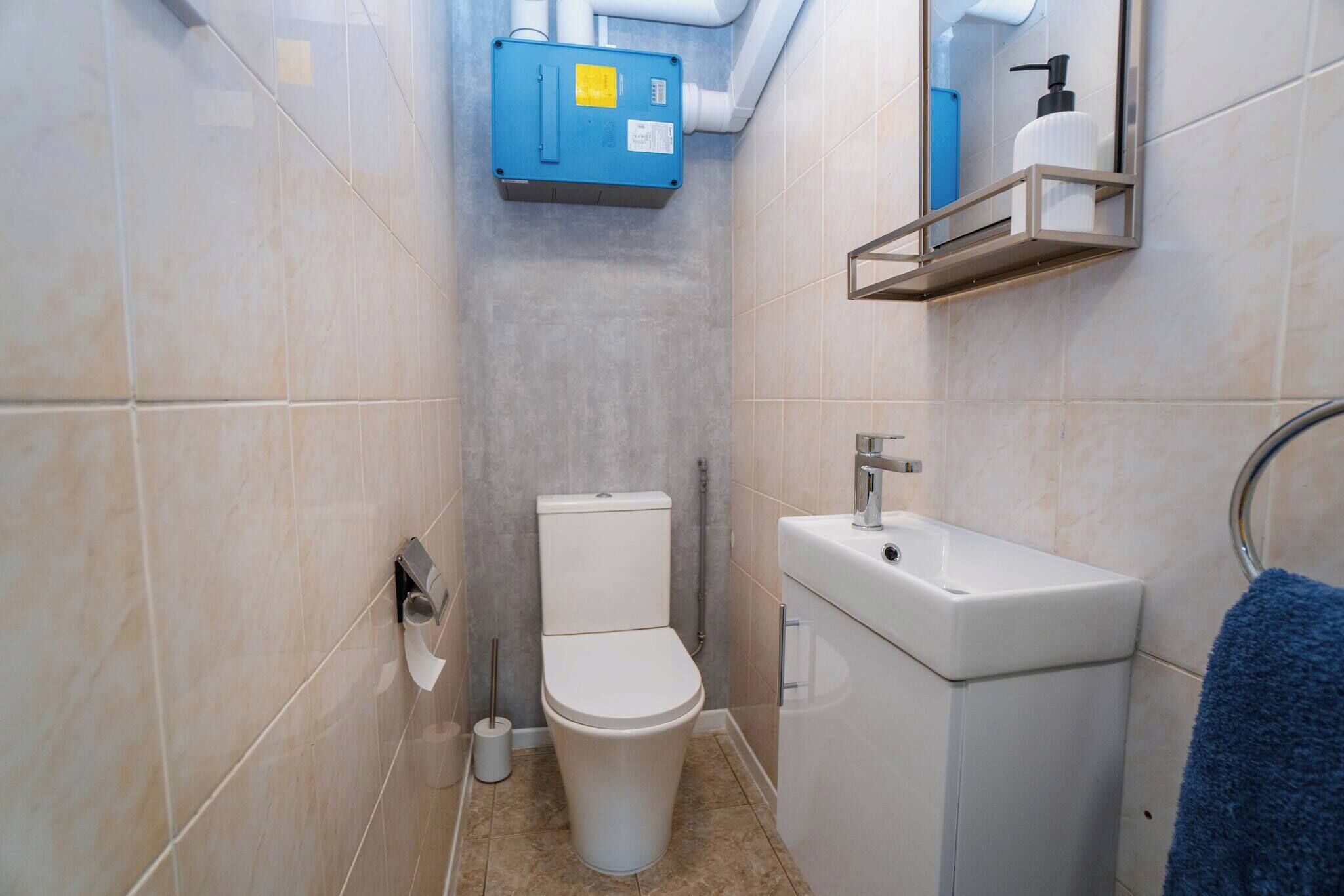 Une petite salle de bain avec des toilettes, un lavabo et une boîte de raccordement bleue fixée au mur.