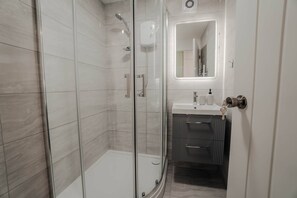 A modern bathroom with a glass shower enclosure, a vanity with a mirror, and a sink. - Free Parking 2BR Sleeps 5 Close to JR Hospital (Oxford)
