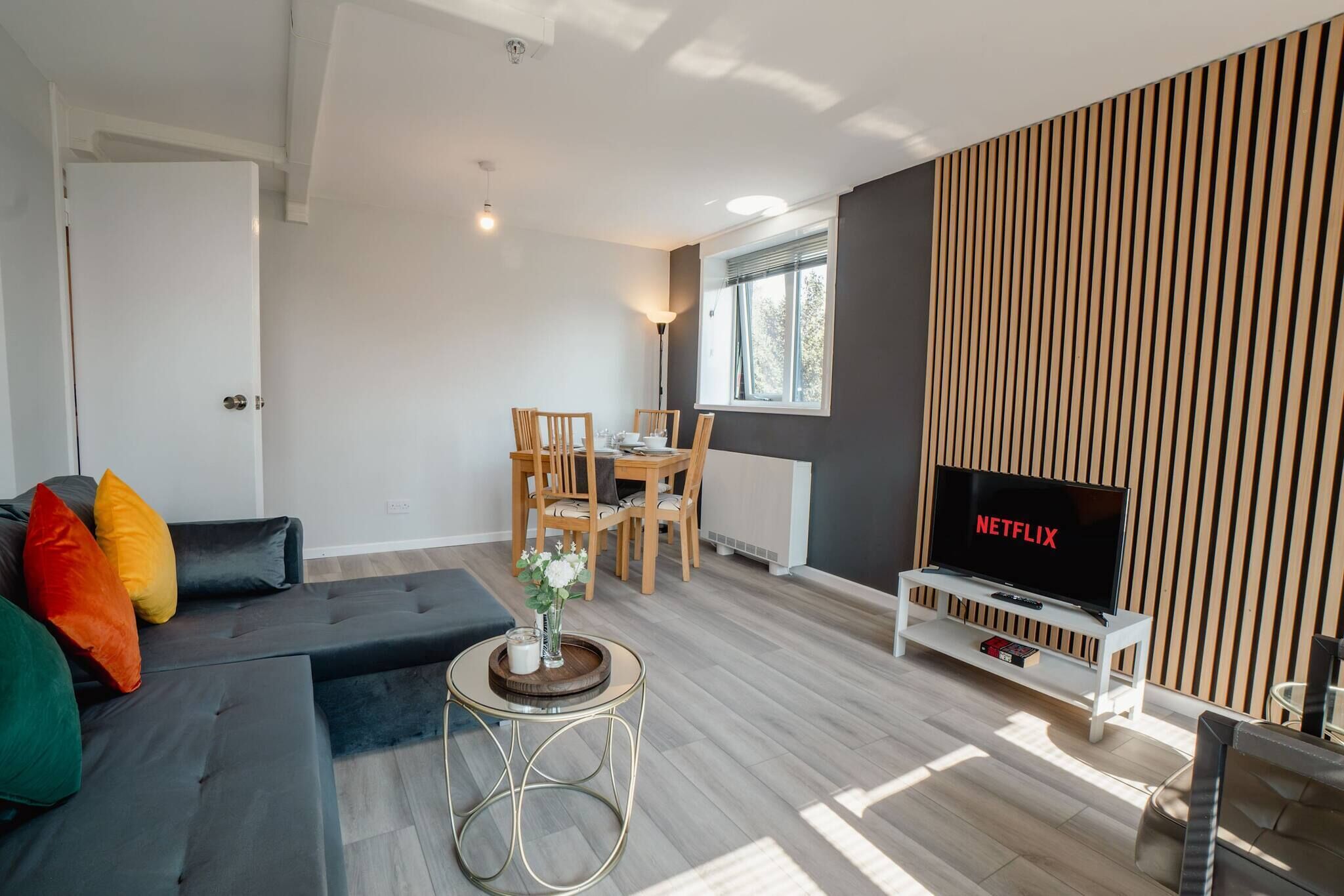 A modern living room with a sofa, a dining table, chairs, a TV, and a decorative vase.