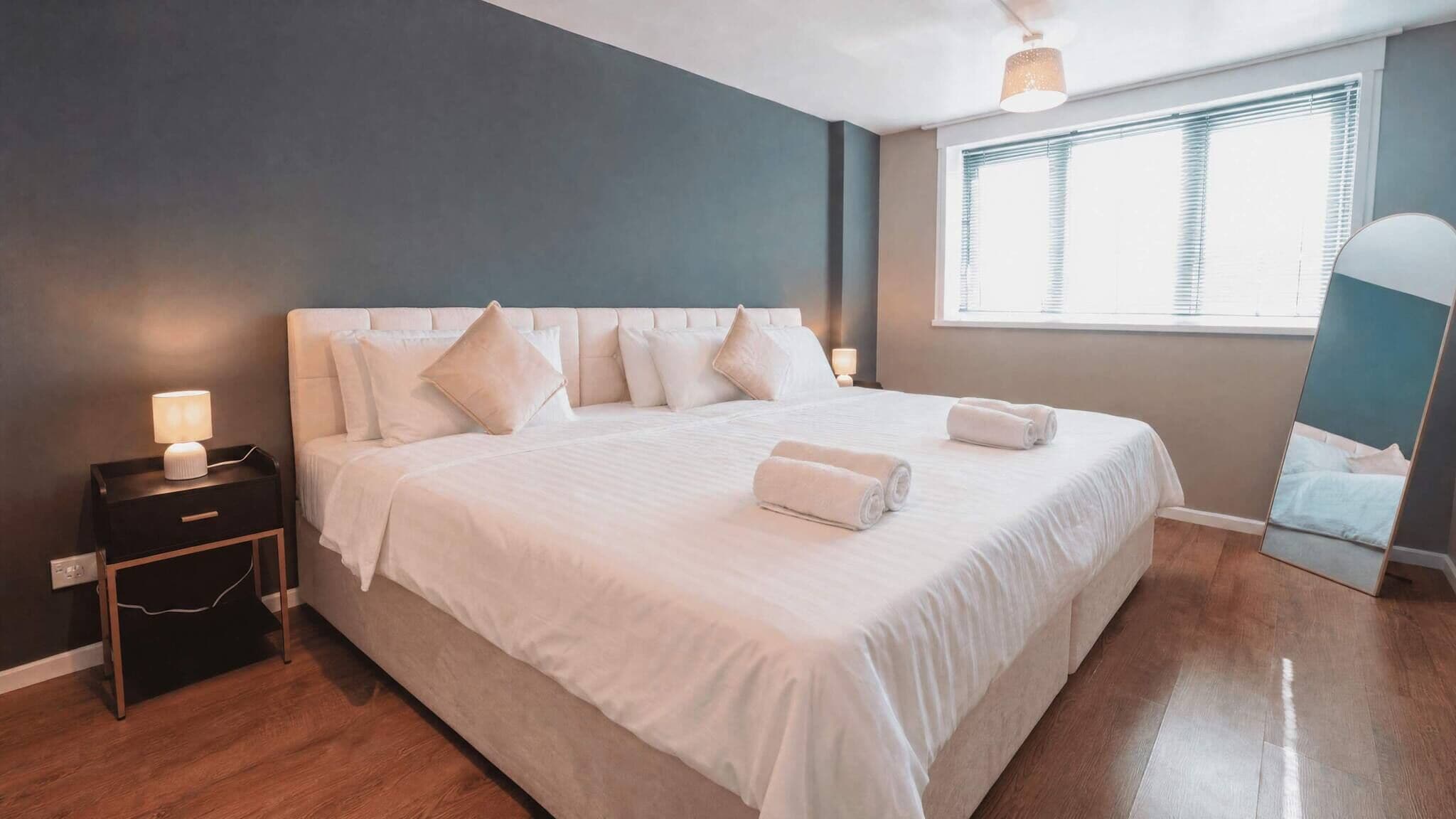 Habitación de hotel con una cama grande, mesitas de noche, una ventana con persianas y un espejo.