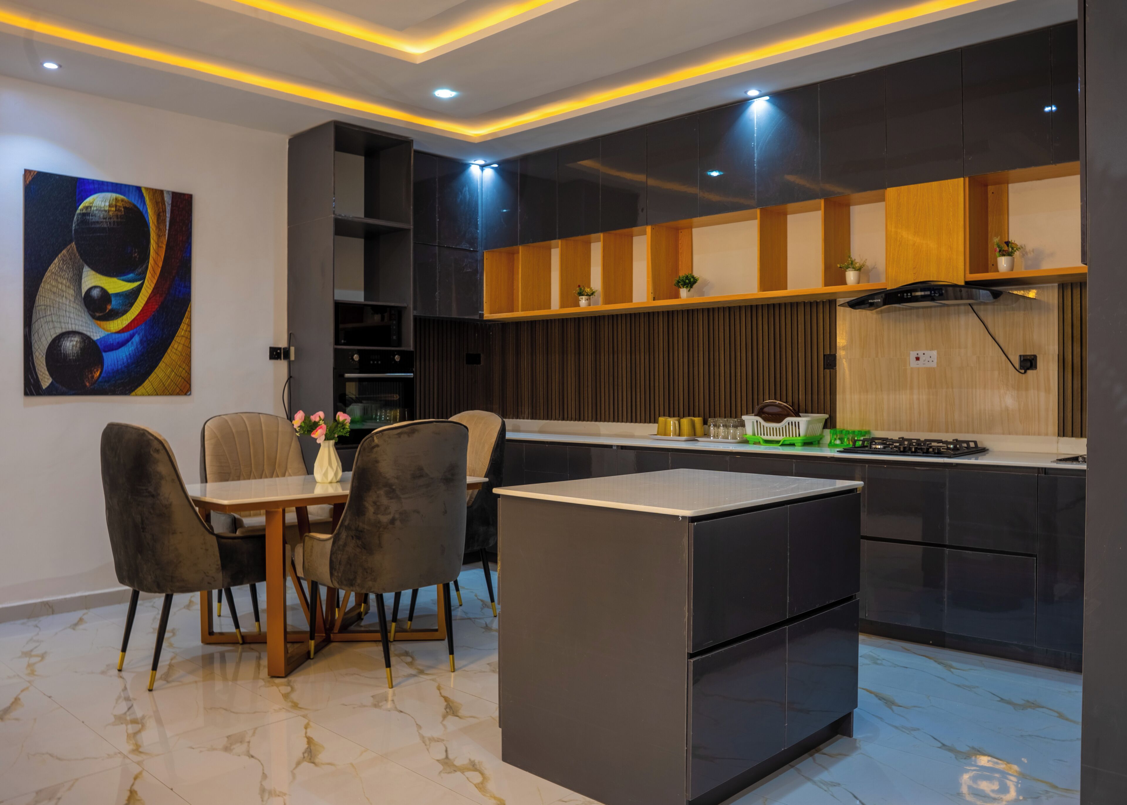A modern kitchen with a dining area, featuring a marble floor, contemporary furniture, and a large painting on the wall.