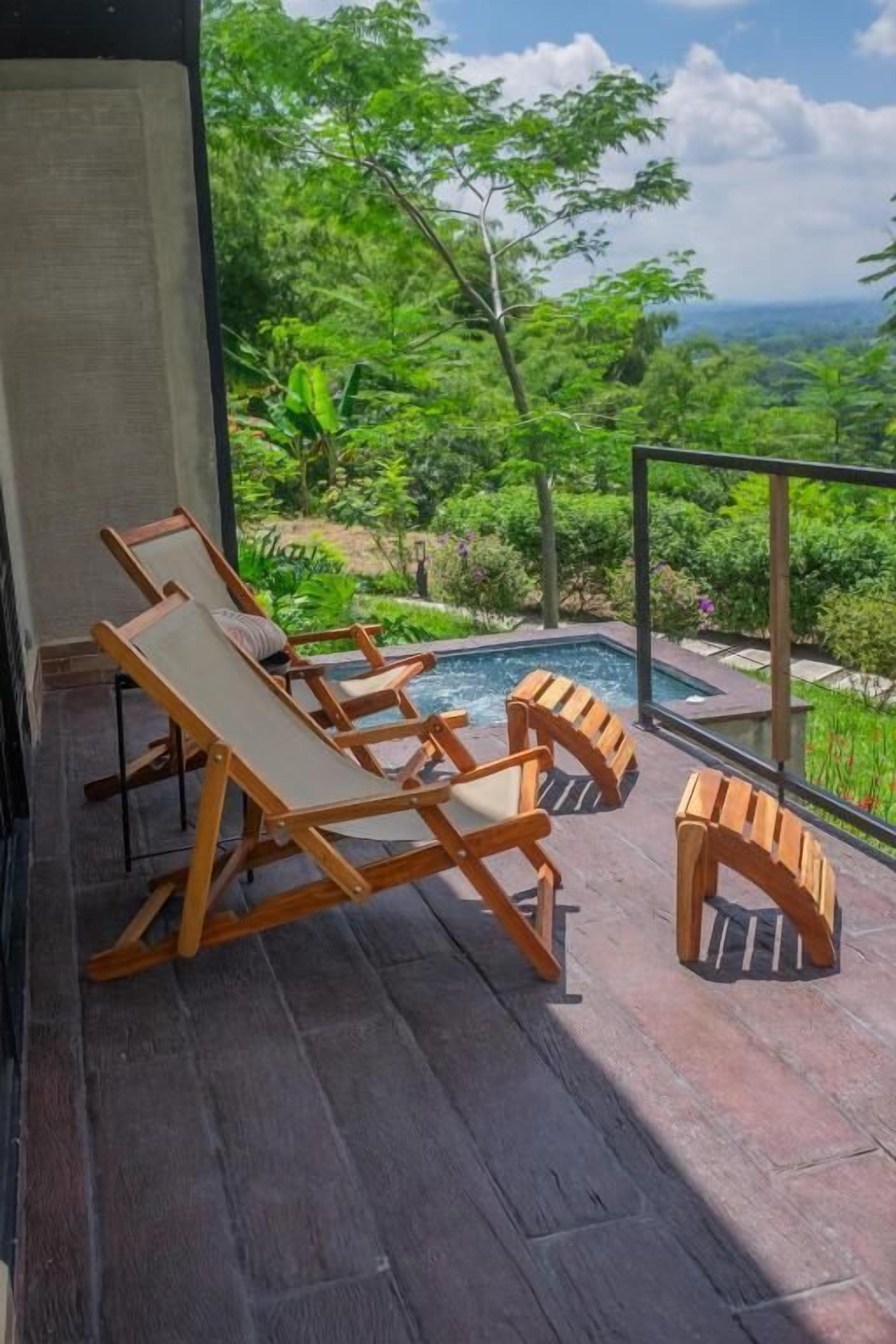 Eine Holzterrasse mit Liegestühlen mit Blick auf einen Pool und üppiges Grün.