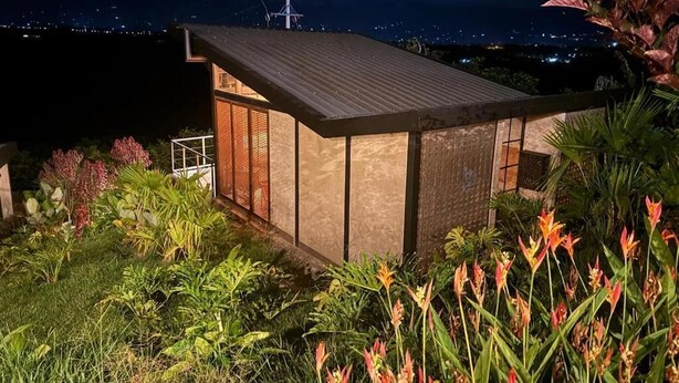 A modern building with a sloped roof, surrounded by lush greenery and flowering plants.