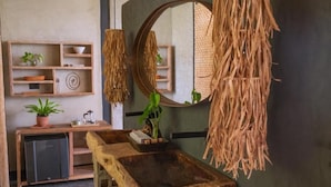 A rustic bathroom with a wooden sink, a mirror, and a shelf with plants.