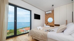 A bedroom with a large window, a bed, a flat-screen TV, and a wooden wardrobe. - Villa Rovni (Rasa)