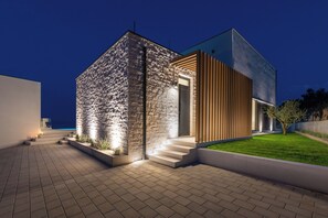 Ein modernes, zweistöckiges Haus mit Natursteinfassade und Holzverkleidung, mit gut beleuchtetem Eingangsbereich und gepflasterter Auffahrt.