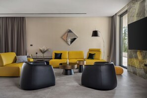 Ein modernes Wohnzimmer mit einer Sofagarnitur, schwarzen Hocker, einem Couchtisch und einer Wandlampe.