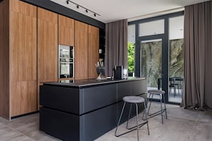 A modern kitchen with wooden cabinets, a black countertop, and a large island with stools. - Villa She Luxury (Groznjan)