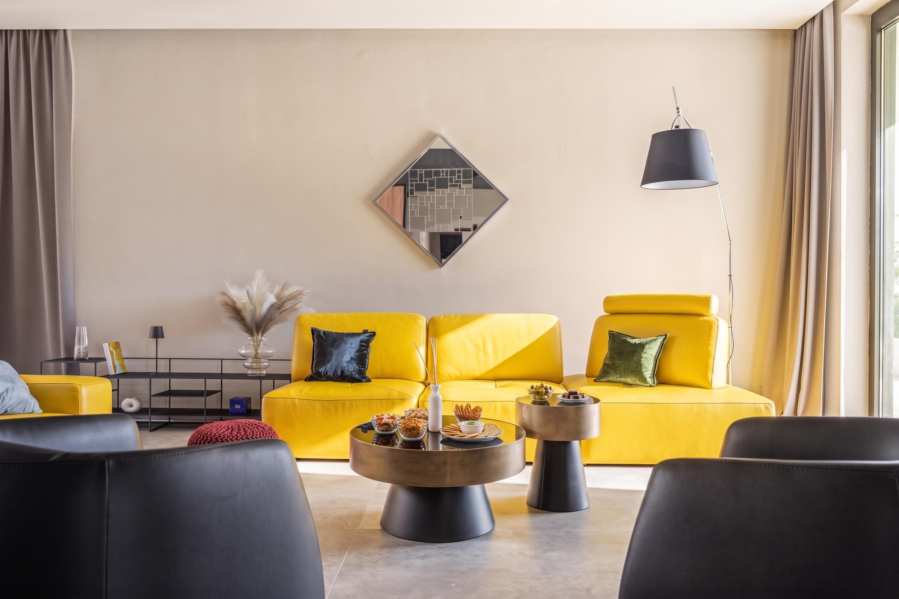 A modern living room with a yellow sofa, black armchairs, a round coffee table, and a side table.