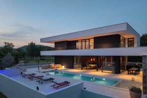 Ein modernes, zweistöckiges Haus mit Pool, Sitzgelegenheiten im Freien und Essbereich.