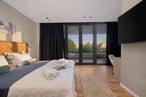 Een moderne slaapkamer met een groot bed, een flatscreen televisie en uitzicht op de omgeving via een schuifdeur.