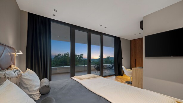 A modern bedroom with a large bed, a flat-screen TV, a balcony with a view, and a wooden cabinet. - Villa She Luxury (Groznjan)