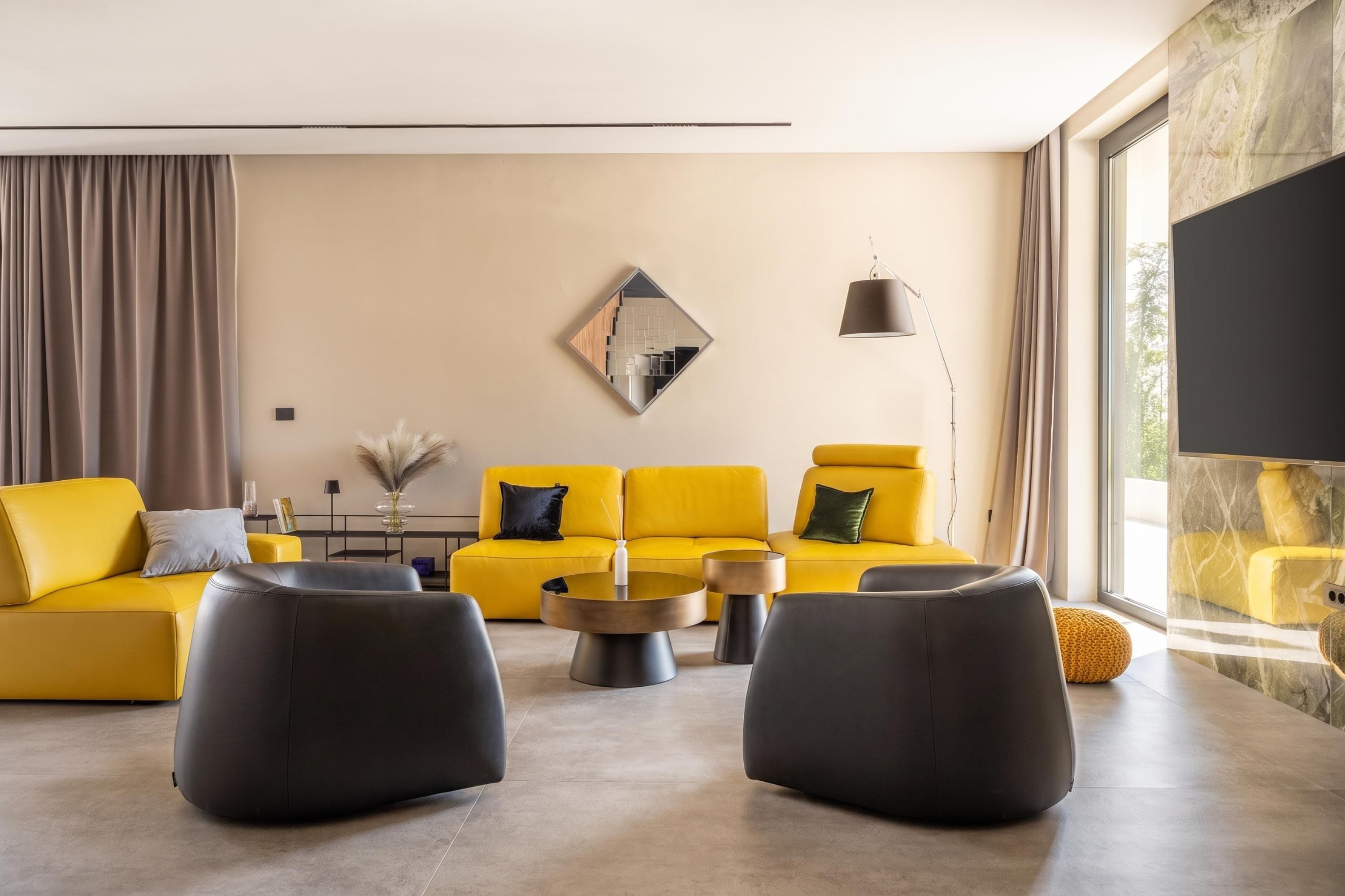 A modern living room with a yellow sofa set, black ottomans, and a large mirror on the wall.