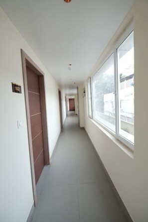Corredor com portas numeradas 102, dando acesso a quartos com grandes janelas.