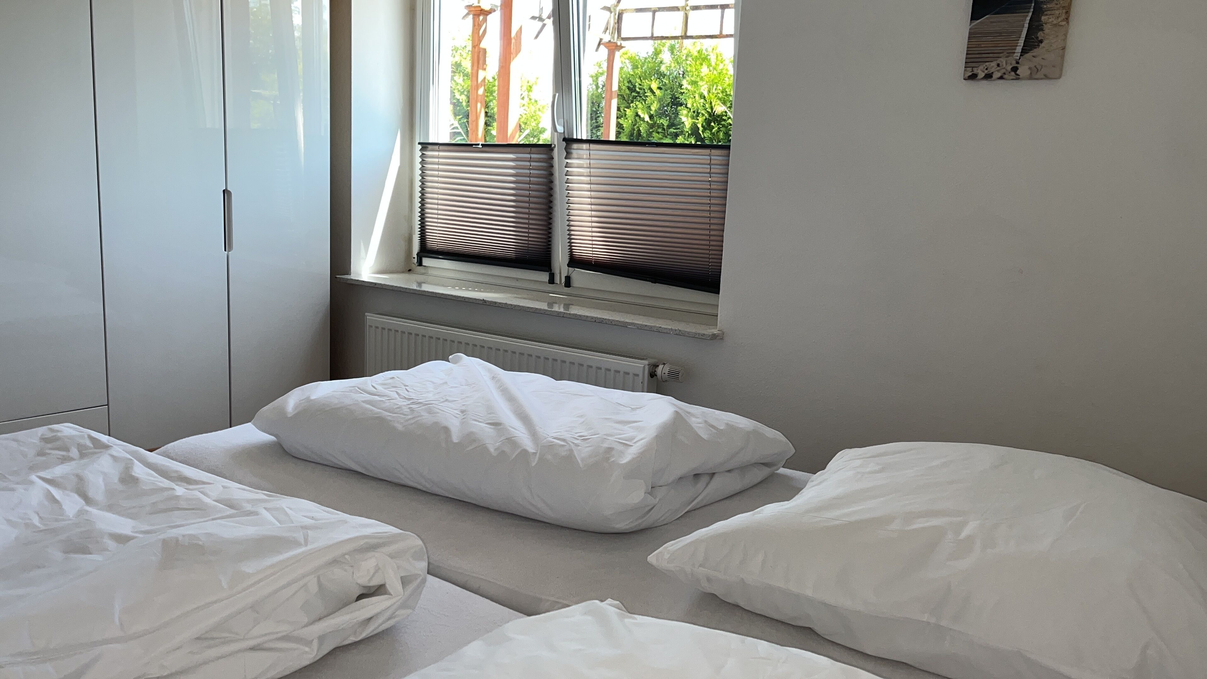 A bedroom with two beds, a radiator, and a window with blinds.