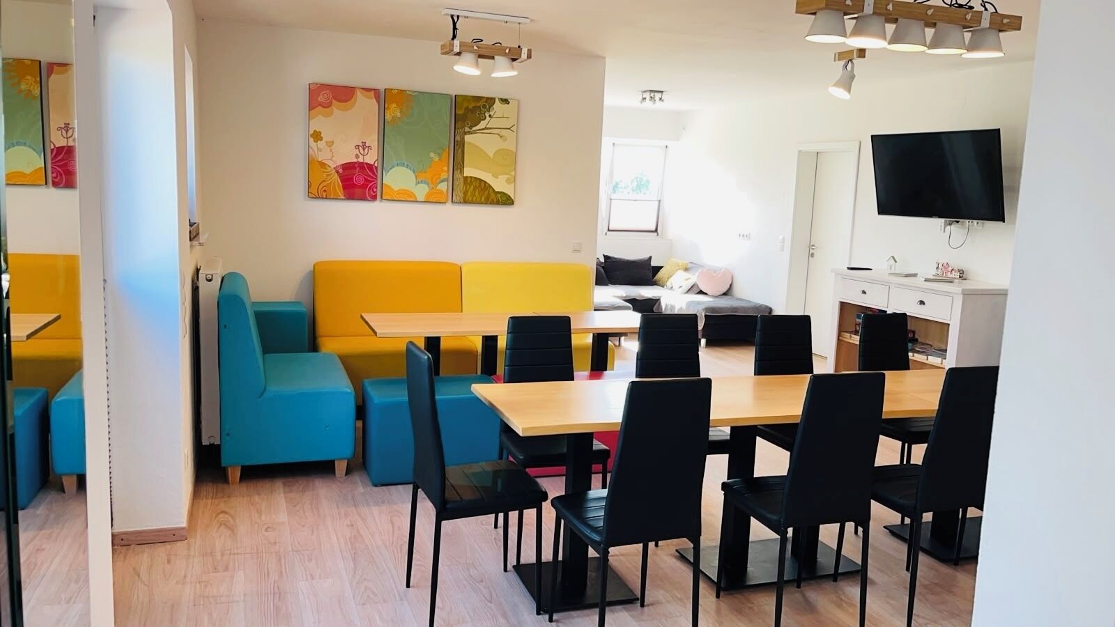 Un coin repas avec une table en bois et des chaises noires, un canapé jaune et un téléviseur fixé au mur.